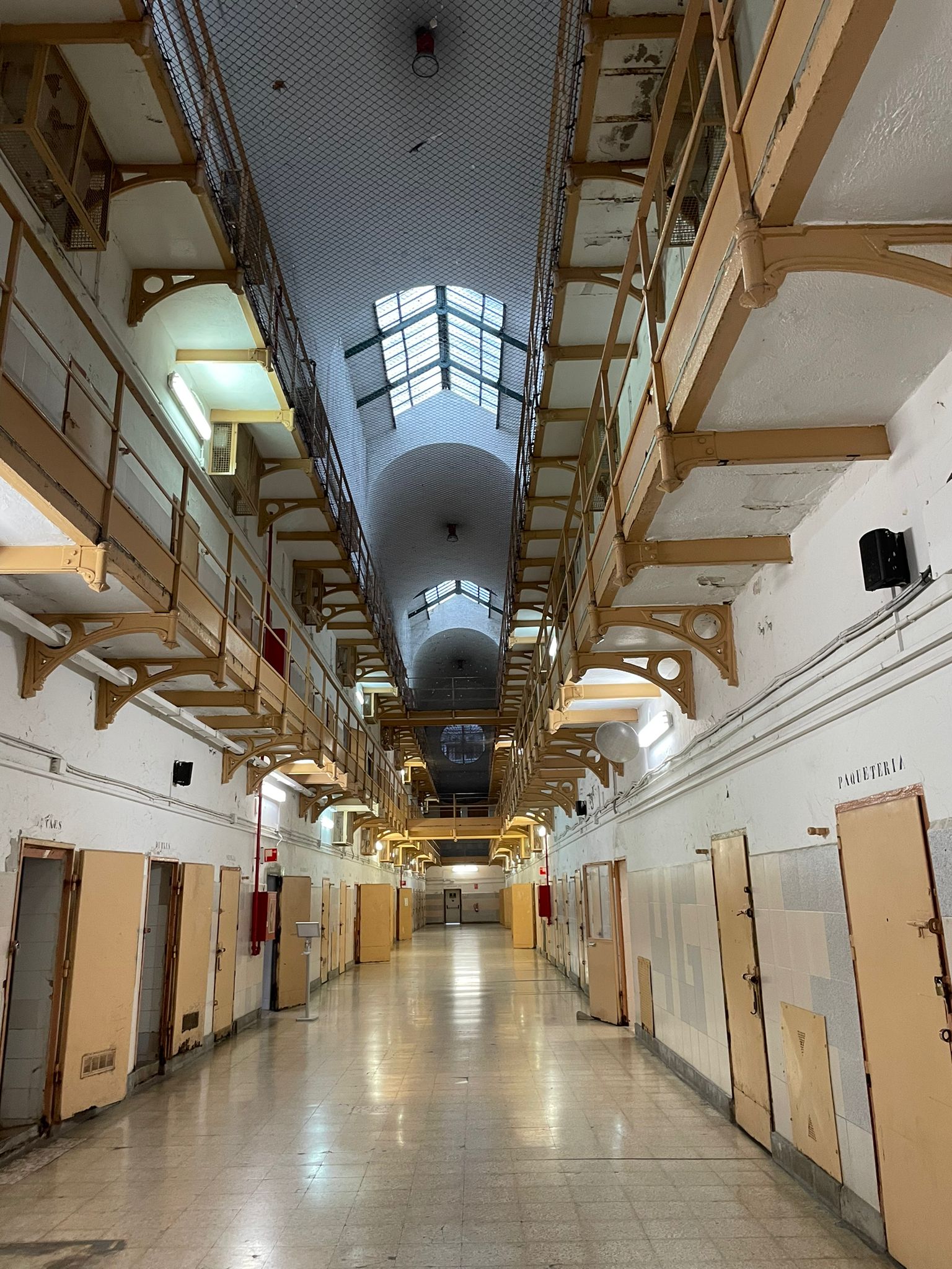 Interior view of a former prison's hallway with cells on either side and a skylight ceiling.